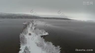 航拍越野驾驶缓慢沿着狭窄的雪岛道路在湖或河冬季景观与